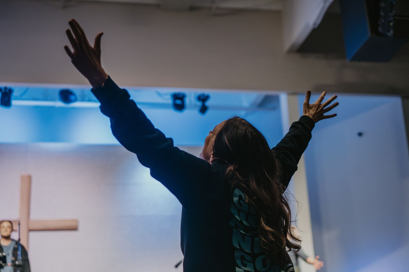 A woman on stage with both arms raised under blue light
